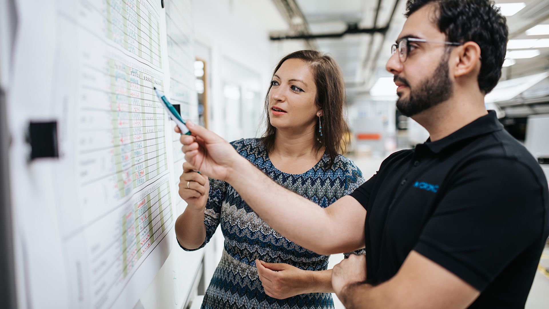 One male and one female Mycronic colleague cooperating in front of a whiteboard